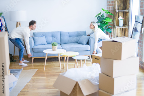 Young beautiful couple moving sofa at new home around cardboard boxes