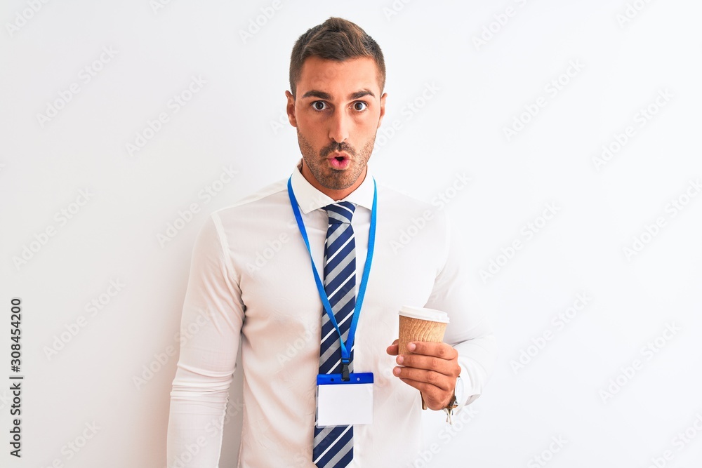Young handsome business man wearing id pass and drinking coffee over isolated background scared in shock with a surprise face, afraid and excited with fear expression Young handsome business man wearing id pass and drinking coffee over isolated background scared in shock with a surprise face, afraid and excited with fear expression