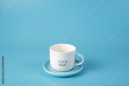 White Cup on a saucer with inscription on blue background. Conveys freshness, vivacity.