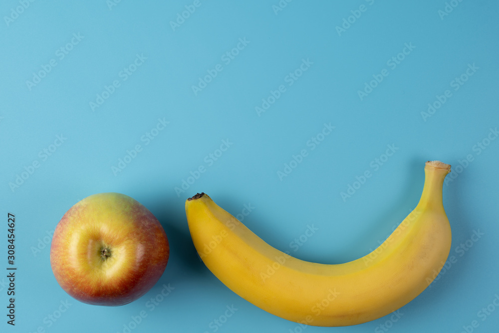 Yellow Banana and red Apple on blue background, top view. The concept of a healthy lifestyle, nutrition.