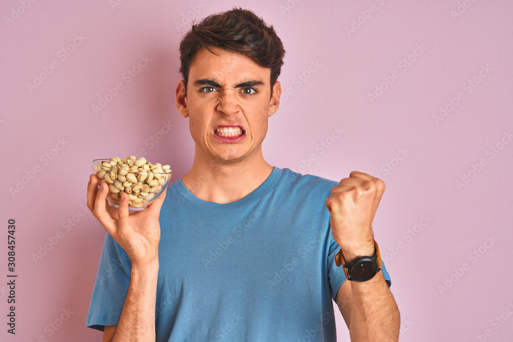 Teenager boy holding a bunch of pistachios over isolated pink background annoyed and frustrated shouting with anger, crazy and yelling with raised hand, anger concept Teenager boy holding a bunch of pistachios over isolated pink background annoyed and frustrated shouting with anger, crazy and yelling with raised hand, anger concept