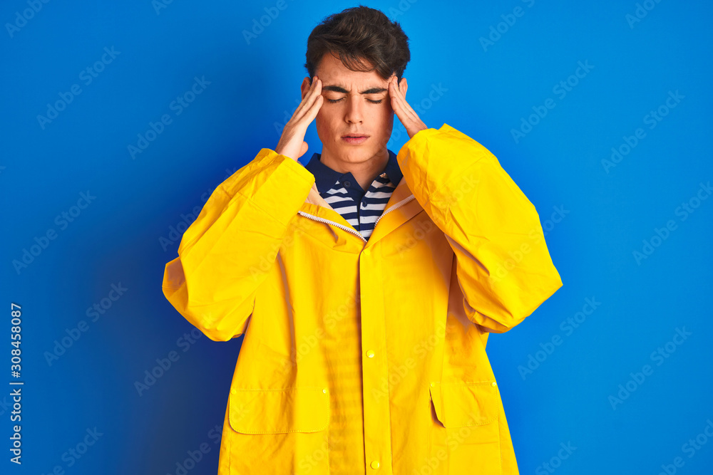 Teenager fisherman boy wearing yellow raincoat over isolated background with hand on head for pain in head because stress. Suffering migraine.