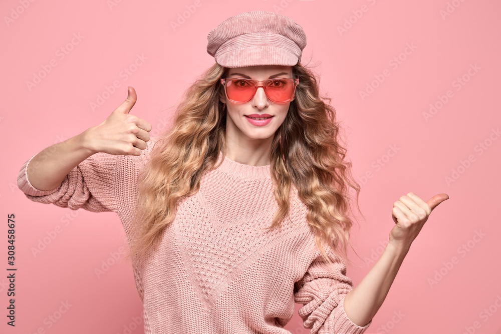 Easy-going Woman happy smiling in Stylish fashion pink colored outfit. Beautiful young Girl in Trendy jumper, make up. Joyful blonde lady shows yes sign in pink cap, fashionable happiness concept Easy-going Woman happy smiling in Stylish fashion pink colored outfit. Beautiful young Girl in Trendy jumper, make up. Joyful blonde lady shows yes sign in pink cap, fashionable happiness concept