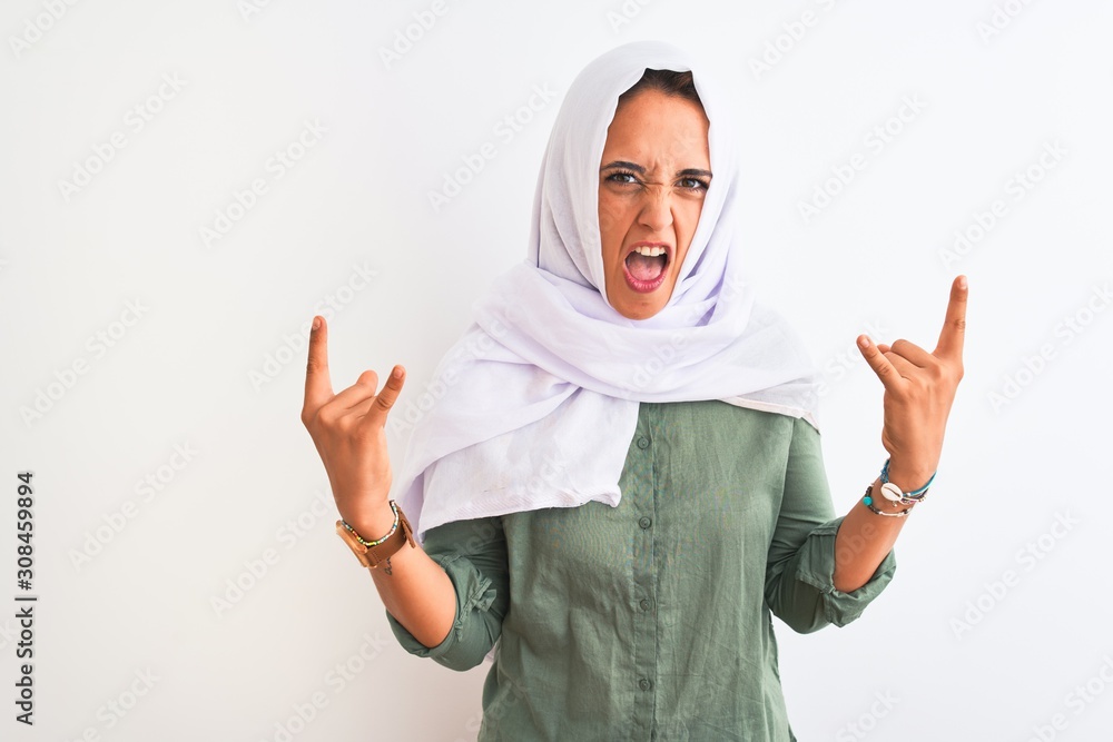 Young beautiful Arab woman wearing traditional Muslim hijab over isolated background shouting with crazy expression doing rock symbol with hands up. Music star. Heavy concept.