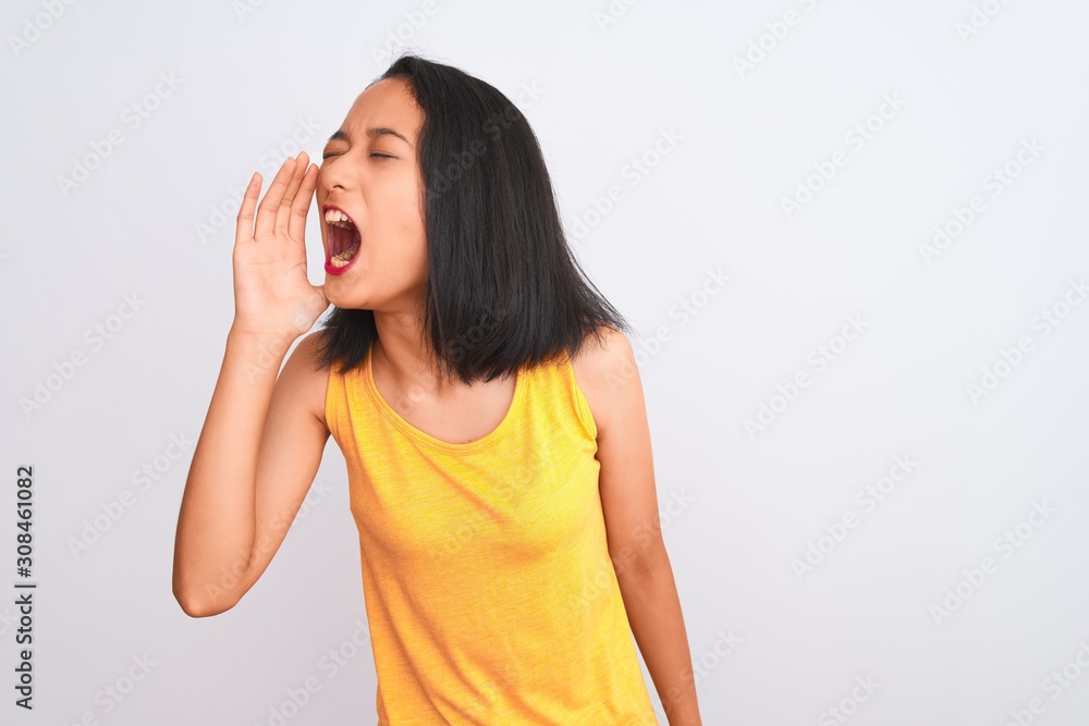 Young chinese woman wearing yellow casual t-shirt standing over isolated white background shouting and screaming loud to side with hand on mouth. Communication concept. Young chinese woman wearing yellow casual t-shirt standing over isolated white background shouting and screaming loud to side with hand on mouth. Communication concept.