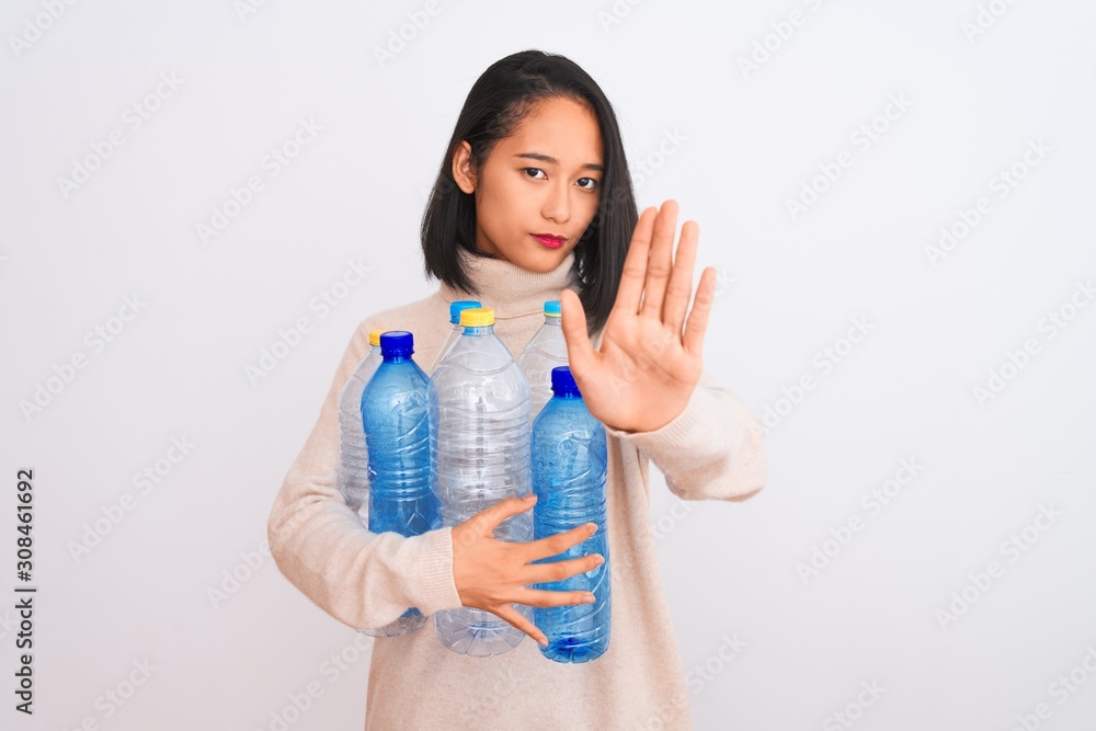 Young beautiful chinese woman recycling plastic bottles over isolated white background with open hand doing stop sign with serious and confident expression, defense gesture Young beautiful chinese woman recycling plastic bottles over isolated white background with open hand doing stop sign with serious and confident expression, defense gesture