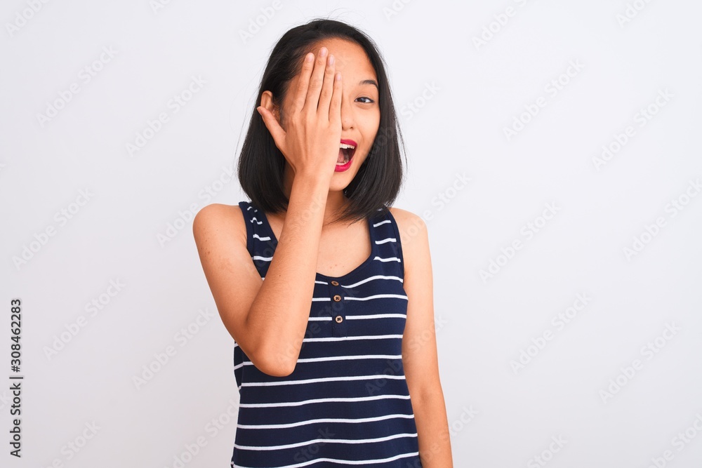 Young chinese woman wearing striped t-shirt standing over isolated white background covering one eye with hand, confident smile on face and surprise emotion. Young chinese woman wearing striped t-shirt standing over isolated white background covering one eye with hand, confident smile on face and surprise emotion.