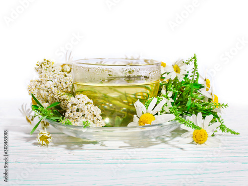 Herbal tea with chamomile and common yarrow in a glass cup with fresh herbs on white wooden background