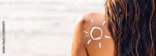 Woman wearing two piece bikini applying suncream with sun drawn on back on the tropical beach.Summer vacations