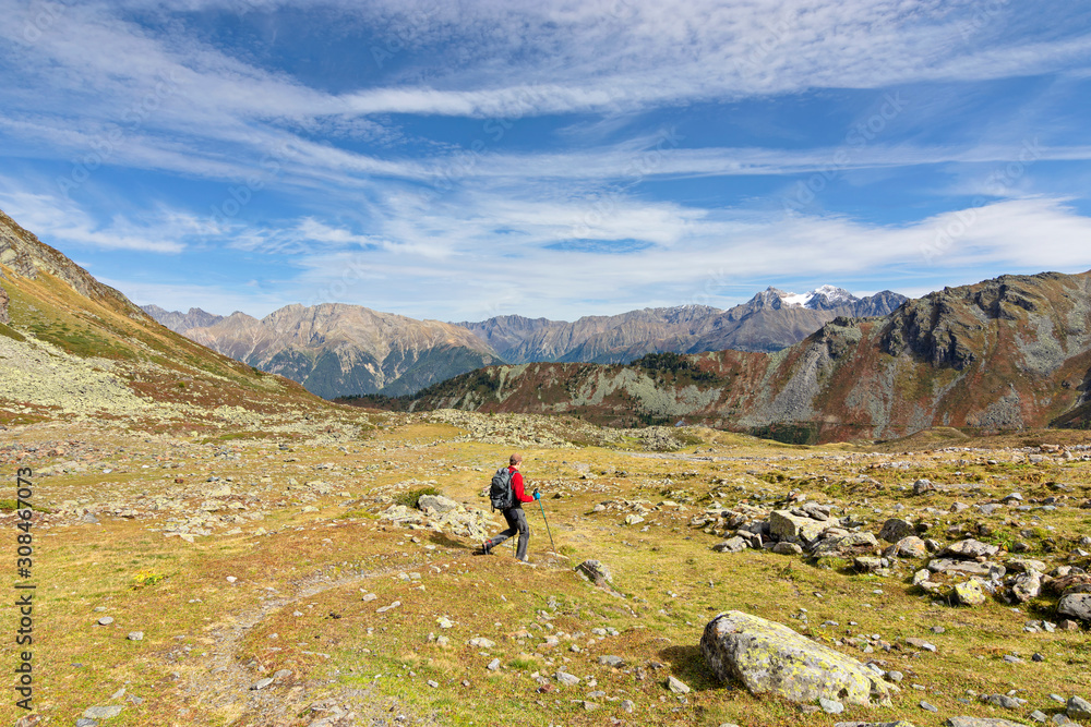Male hiker in autumn walking in the Oetztal Alps, Tirol, Austria. Landscape with grass, rocky mountains and blue sky