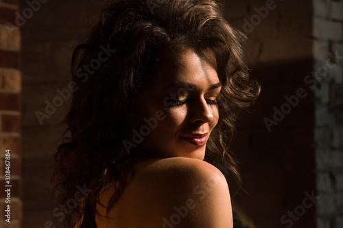 Close up, macro. Portrait of sensual pin-up model with a naked rounded shoulder. Brown brick wall in the background.