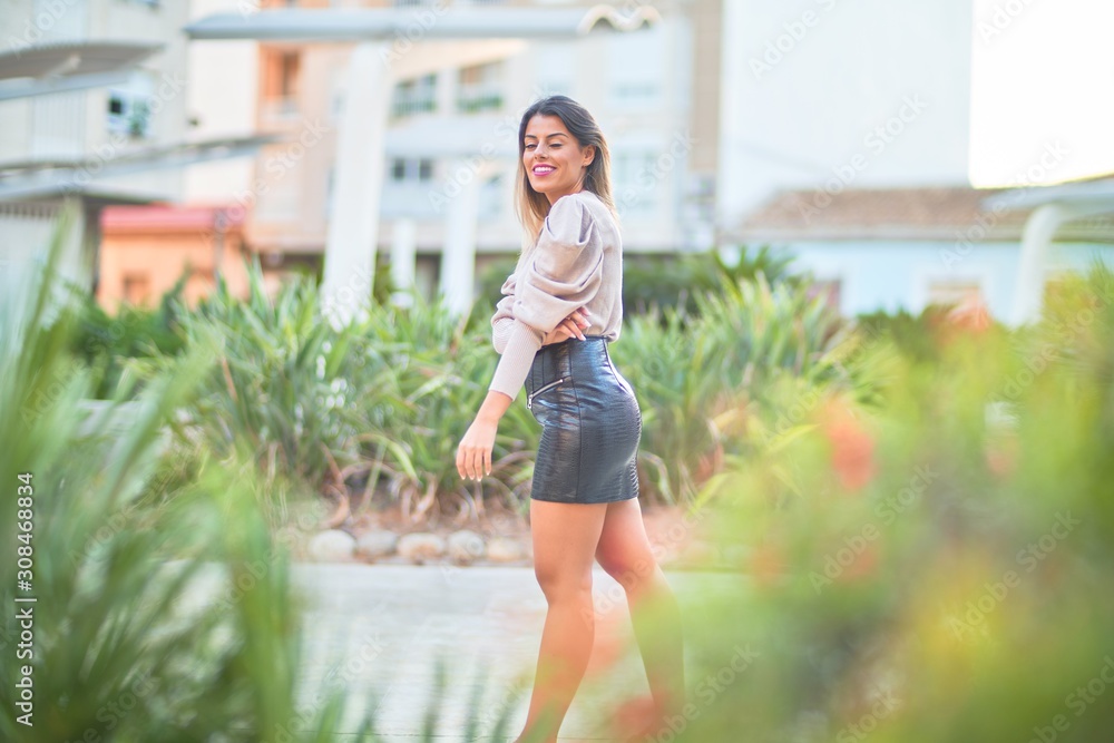 Young beautiful woman wearing sweater and skirt smiling happy and confident. Standing with smile on face at the town street
