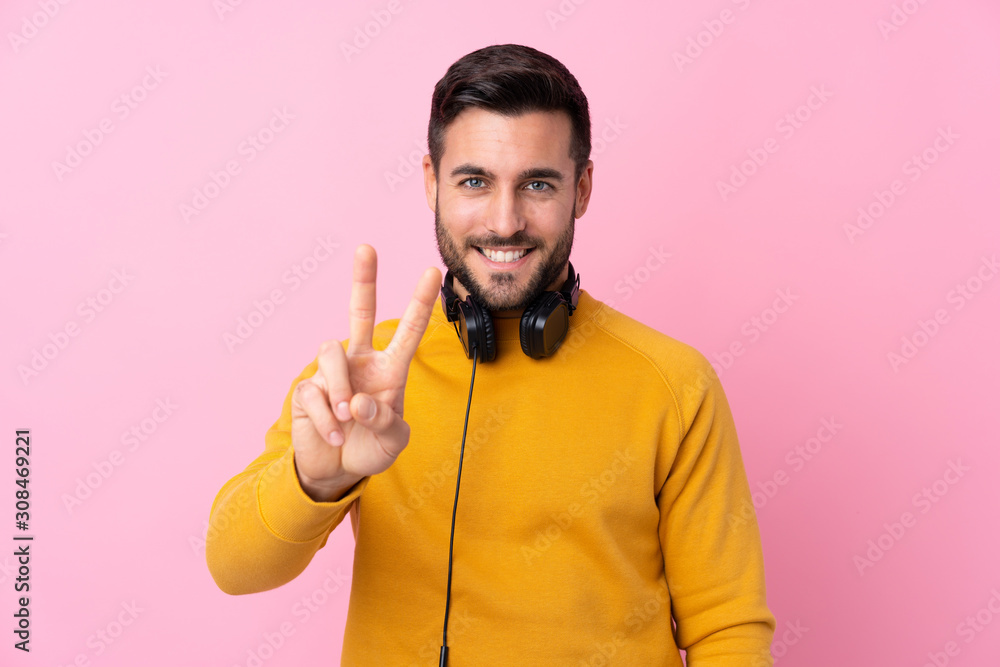 Young handsome man with earphones over isolated pink background smiling and showing victory sign Young handsome man with earphones over isolated pink background smiling and showing victory sign