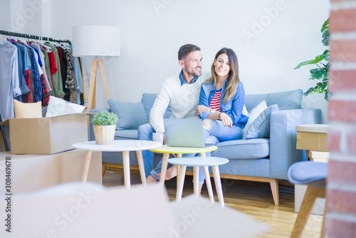 Young beautiful couple sitting on the sofa drinking cup of coffee using laptop at new home around cardboard boxes © Krakenimages.com