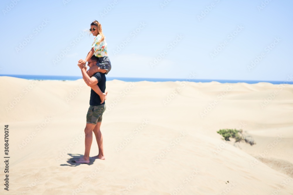 Young beautiful couple smiling happy and confident. Woman sitting on man shoulders with smile on face at the beach