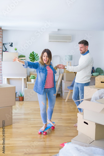 Young beautiful couple playing with skate at new home around cardboard boxes © Krakenimages.com