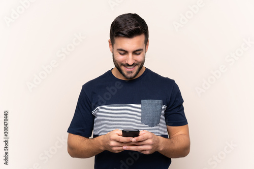 Young handsome man with beard over isolated background sending a message with the mobile © luismolinero