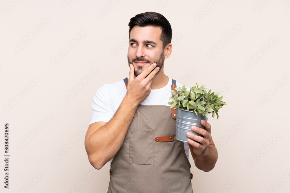 Gardener man holding a plant over isolated background thinking an idea Gardener man holding a plant over isolated background thinking an idea