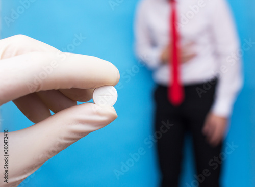 The doctor holds a pill in his hand against the background of a man who has pain and inflammation in his stomach. Concept cure for gastritis and stomach ulcers.