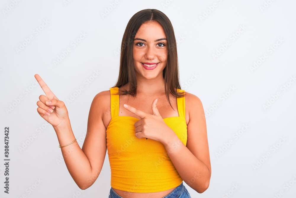 Young beautiful girl wearing yellow casual t-shirt standing over isolated white background smiling and looking at the camera pointing with two hands and fingers to the side. Young beautiful girl wearing yellow casual t-shirt standing over isolated white background smiling and looking at the camera pointing with two hands and fingers to the side.