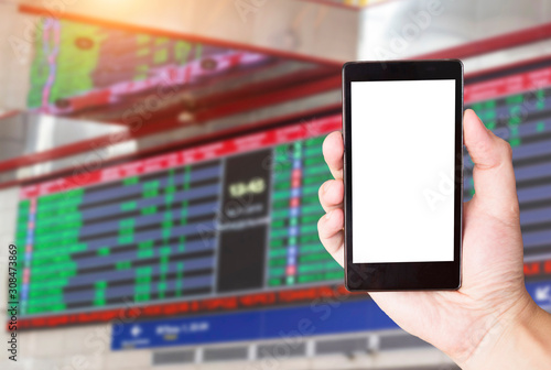 Hand with a mobile phone on the background of an electronic scoreboard of the schedule of buses and railway transport. Concept application for smartphone airport transport and flight schedules