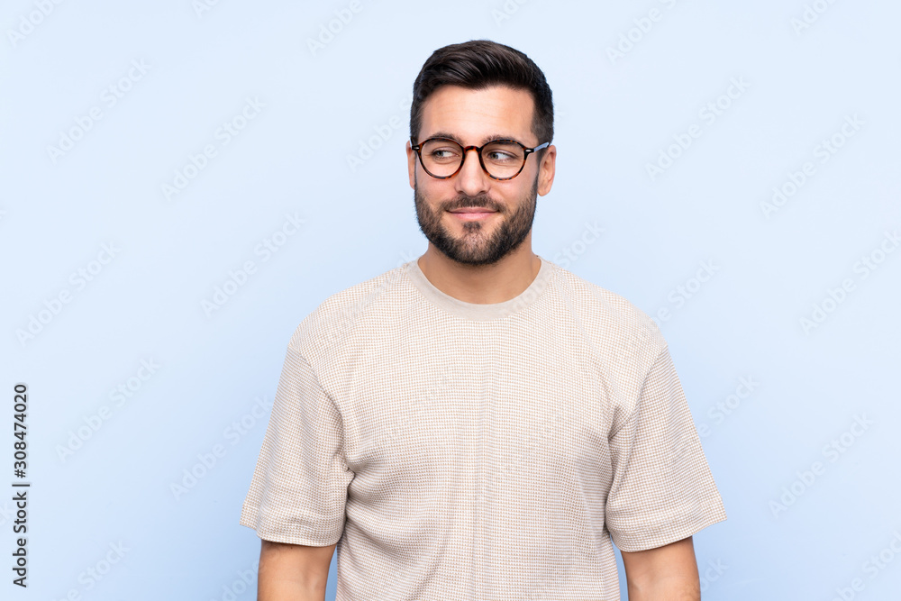 Young handsome man with beard over isolated blue background standing and looking to the side Young handsome man with beard over isolated blue background standing and looking to the side