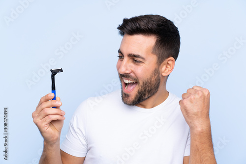 Young handsome man shaving his beard over isolated background celebrating a victory