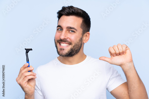 Young handsome man shaving his beard over isolated background proud and self-satisfied