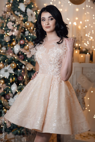 Beauty, make up and people concept - happy laughing young woman. Girl in a beautiful dress. The sexy brunette. Beautiful photo. Sexy brunette girl in evening dress in the fairy Christmas interior. 