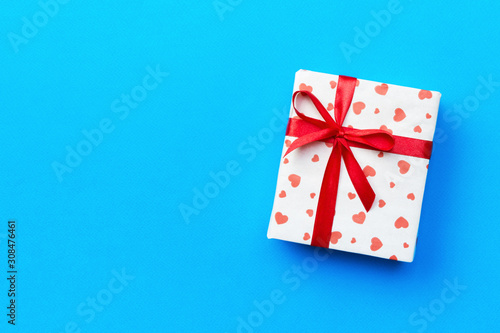 Gift box with red ribbon and heart on blue background, top view with copy space for text