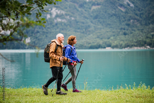 Fototapeta Naklejka Na Ścianę i Meble -  A side view of senior pensioner couple hiking by lake in nature.