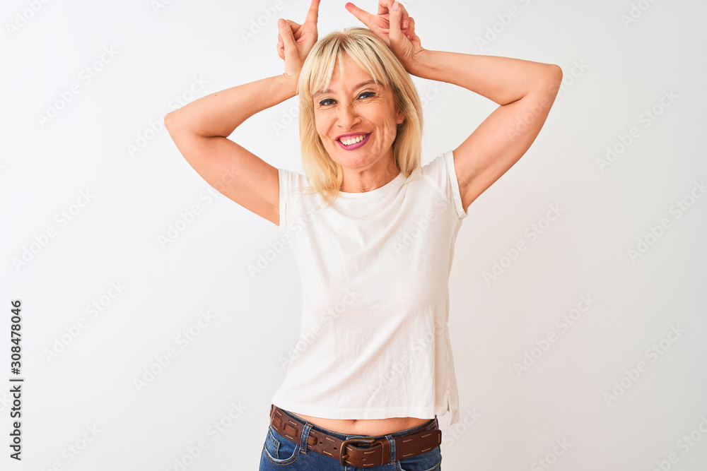 Middle age woman wearing casual t-shirt standing over isolated white background doing funny gesture with finger over head as bull horns Middle age woman wearing casual t-shirt standing over isolated white background doing funny gesture with finger over head as bull horns
