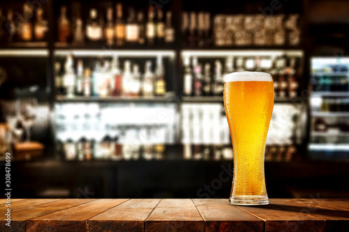 Foto Glass of beer on wooden board and blurred bar background