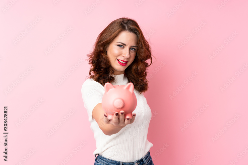 Young Russian woman over isolated pink background holding a big piggybank Young Russian woman over isolated pink background holding a big piggybank