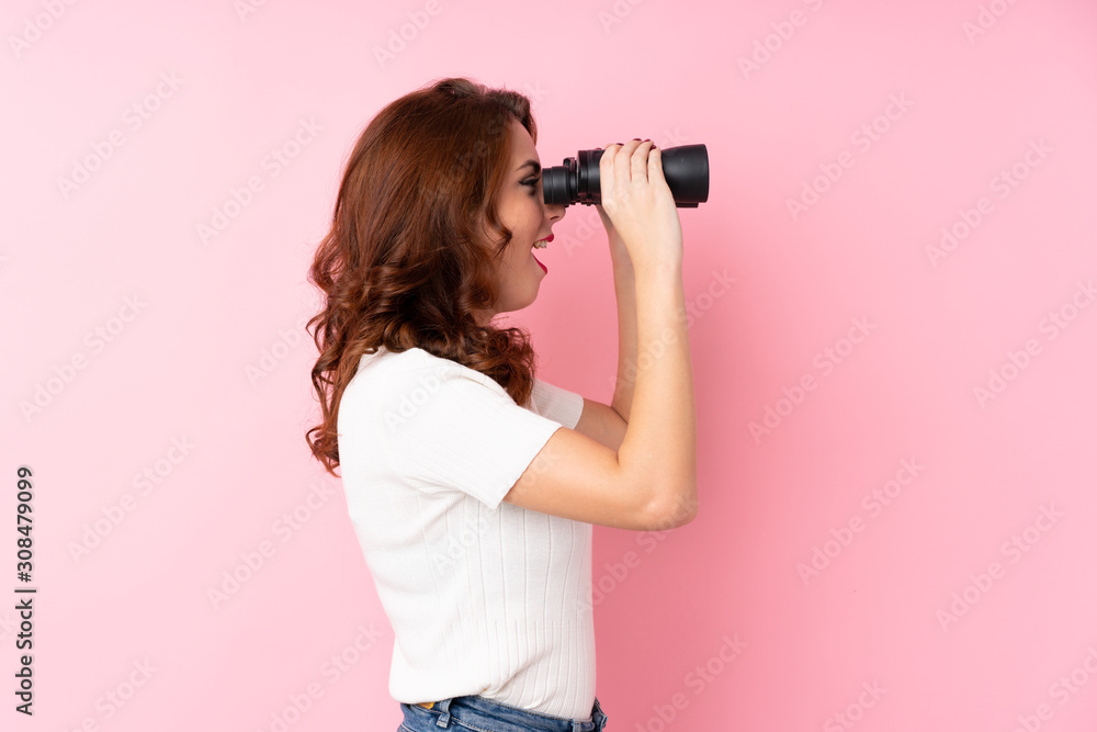 Young Russian woman over isolated pink background with black binoculars Young Russian woman over isolated pink background with black binoculars