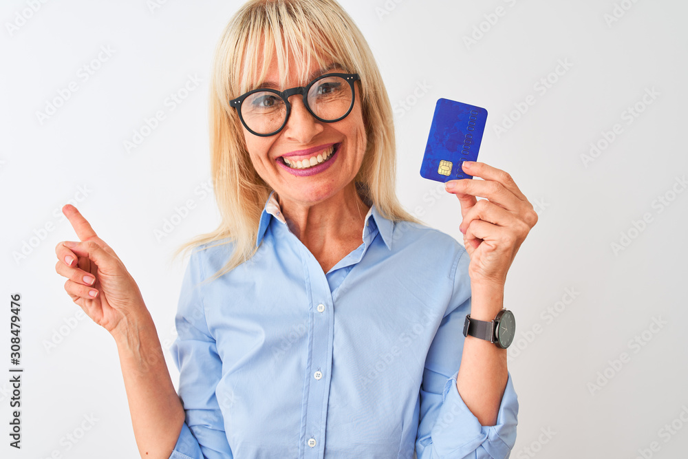 Middle age businesswoman wearing glasses holding credit card over isolated white background very happy pointing with hand and finger to the side Middle age businesswoman wearing glasses holding credit card over isolated white background very happy pointing with hand and finger to the side