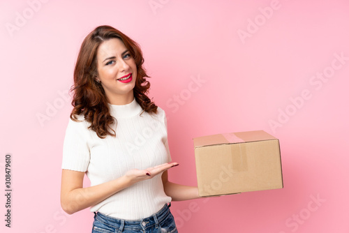 Young Russian woman over isolated pink background holding a box to move it to another site © luismolinero