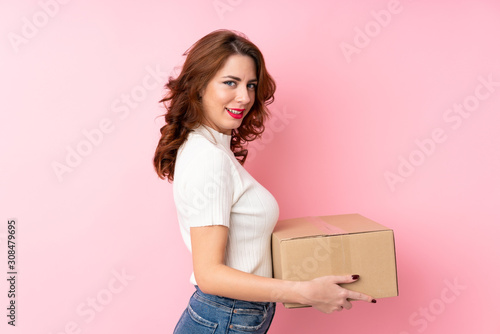 Young Russian woman over isolated pink background holding a box to move it to another site © luismolinero