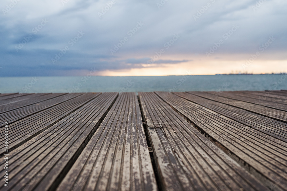View of wooden decking, sea and gray sky at dusk.
