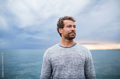Mature man standing outdoors on beach at dusk.