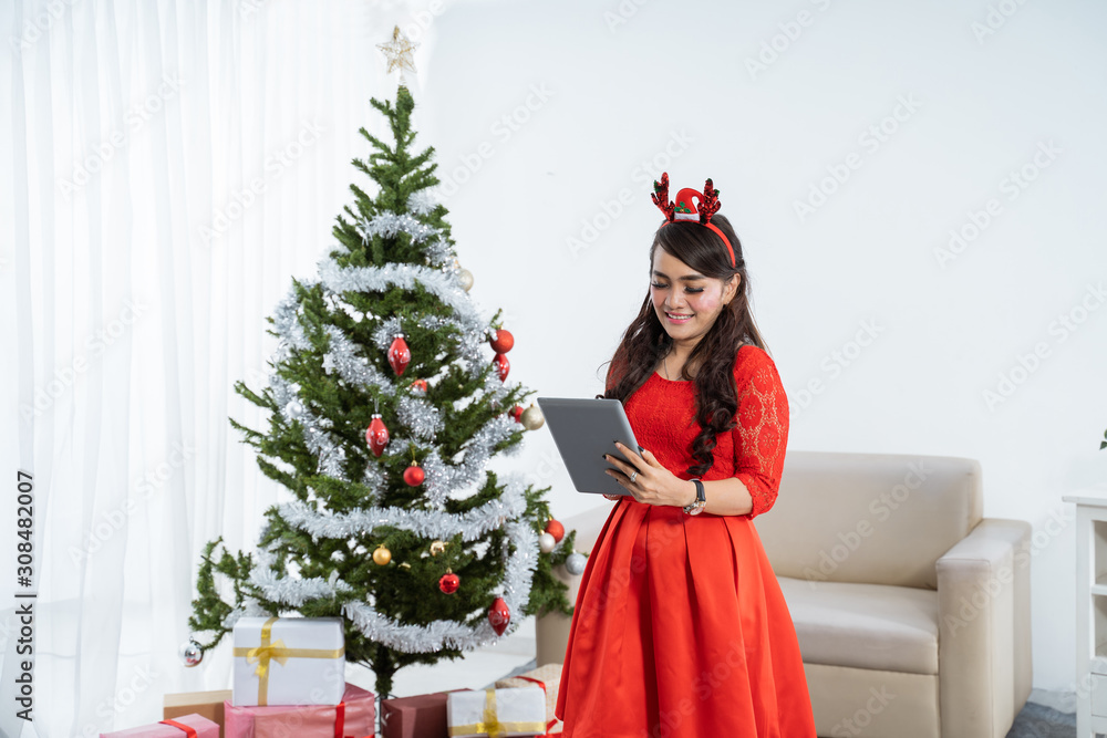 attractive asian woman in red dress using tablet pc on chritstmas day attractive asian woman in red dress using tablet pc on chritstmas day