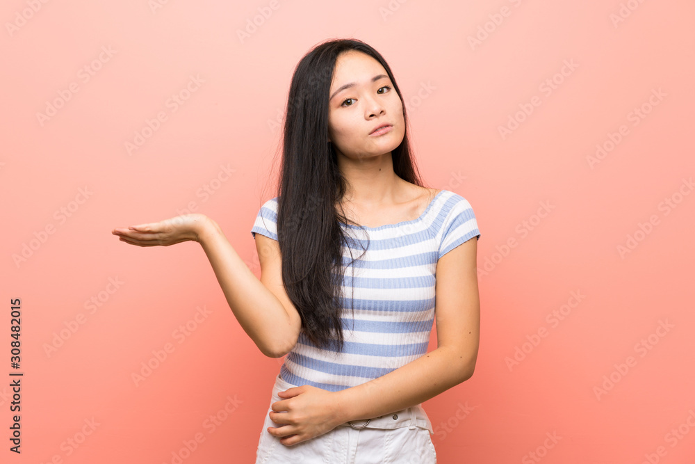 Teenager asian girl over isolated pink background unhappy for not understand something Teenager asian girl over isolated pink background unhappy for not understand something