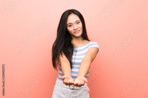 Teenager asian girl over isolated pink background holding copyspace imaginary on the palm to insert an ad