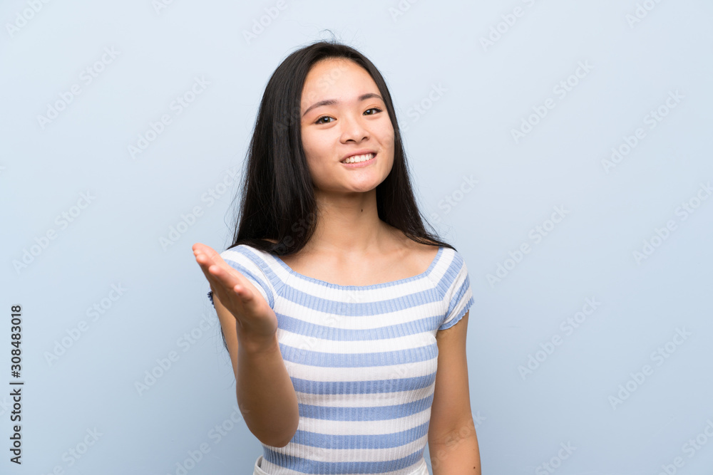 Teenager asian girl over isolated blue background handshaking after good deal Teenager asian girl over isolated blue background handshaking after good deal