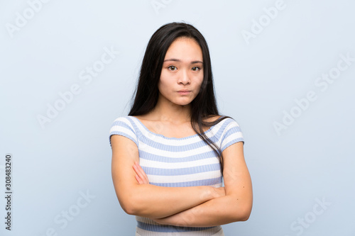 Teenager asian girl over isolated blue background keeping arms crossed