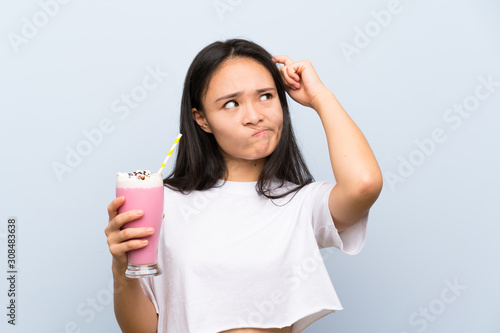 Teenager asian girl holding a strawberry milkshake having doubts and with confuse face expression