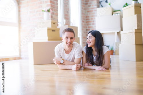 Young beautiful couple lying down at new home around cardboard boxes