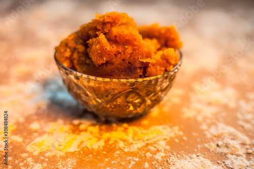 Close up of Indian Gujarati popular dish Atte ka sheera or Halwa-Karah parshad in a glass bowl on brown surface with some spread wheat flour. Horizontal shot. photo