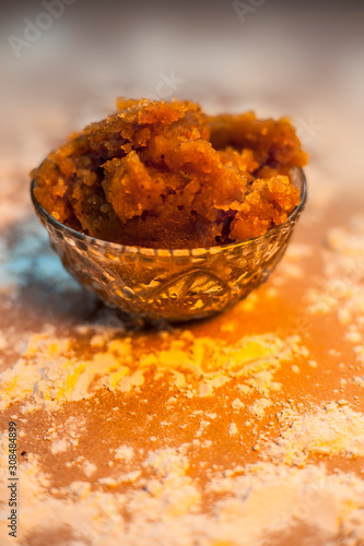 Close up of Indian Gujarati popular dish Atte ka sheera or Halwa-Karah parshad in a glass bowl on a brown surface with some spread wheat flour. Vertical shot. photo