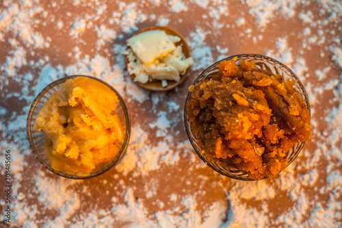 Close up of Indian Gujarati popular dish Atte ka sheera or Halwa-Karah parshad in a glass bowl on a brown surface with some spread wheat flour, jaggery and ghee or clarified butter. photo